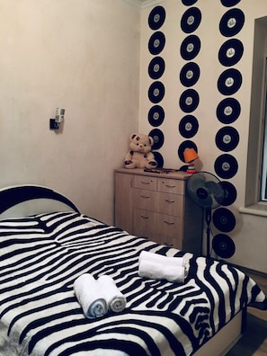 A bedroom with a zebra-striped bedspread, a teddy bear, a lamp, and a wall decorated with vinyl records. - Apartment on Tsamebuli Ave (Tbilisi)