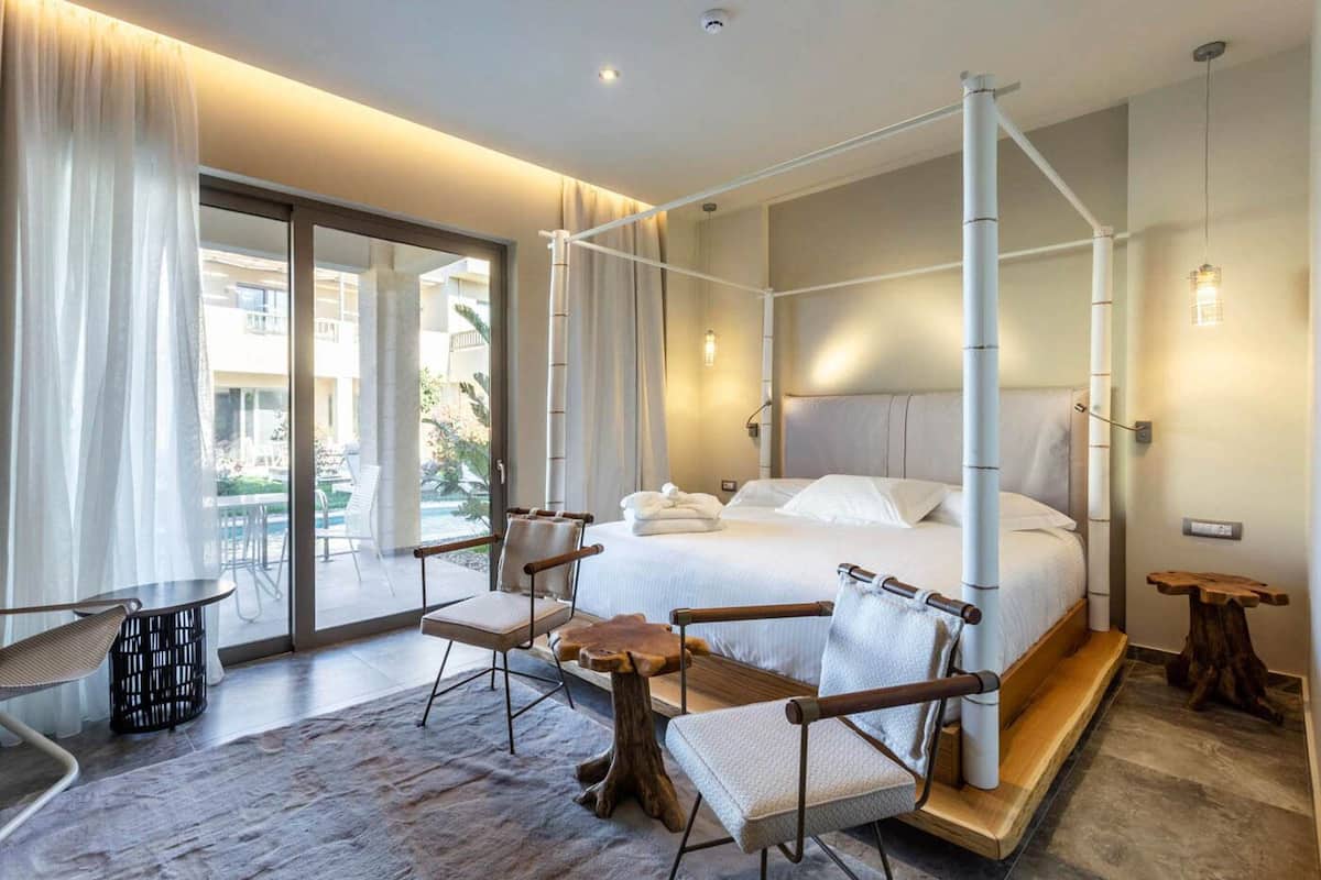 A modern hotel room with a large bed, a balcony, and a seating area with chairs and a table.