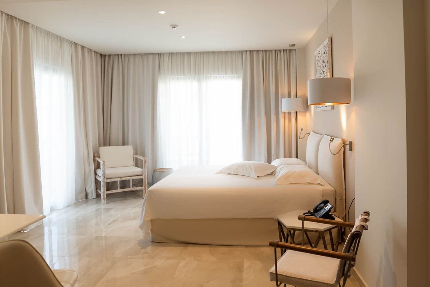A hotel room with a large bed, a chair, a desk, and a lamp.