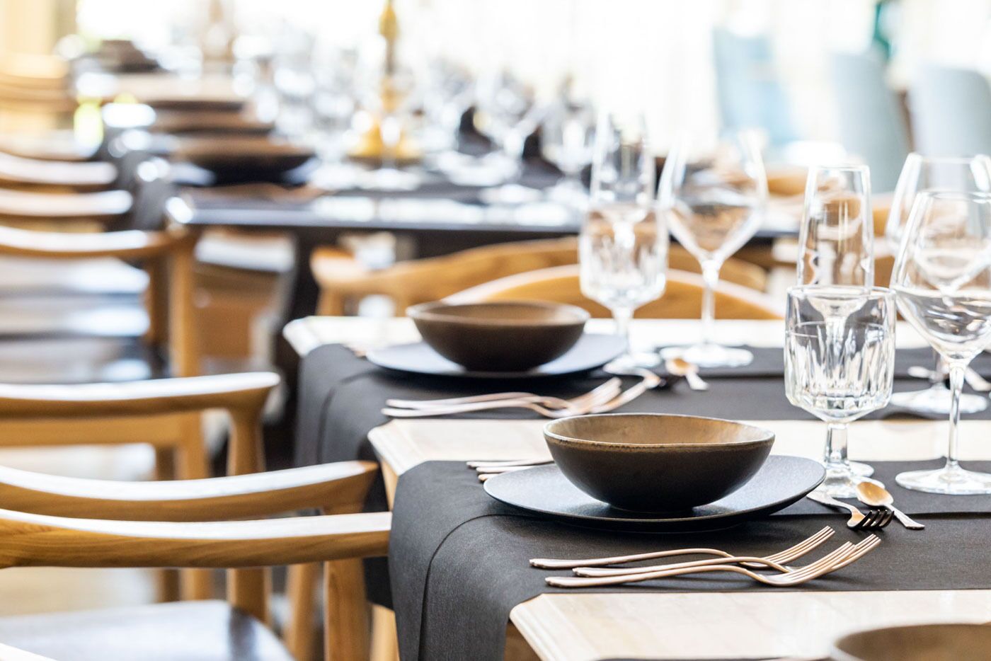 Un restaurante con varias mesas dispuestas para comer, cada una con un tazón, una copa de vino y cubiertos.