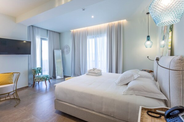 A modern hotel room with a large bed, a desk, a chair, and a TV. - Elysian Luxury Hotel & Spa (Kalamata)
