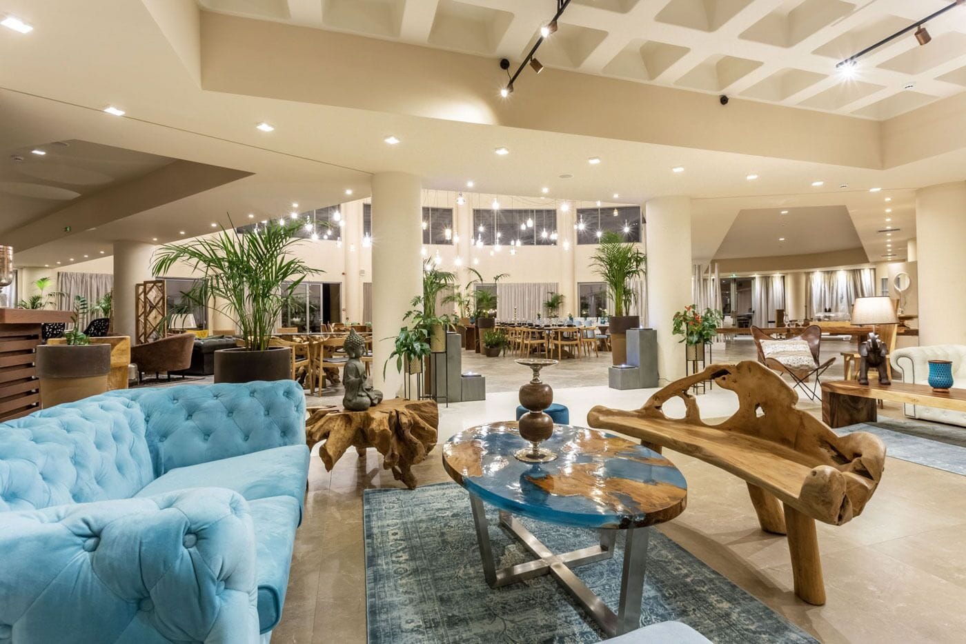 A spacious lobby with a blue sofa, wooden tables, and potted plants.