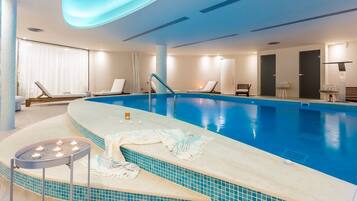 An indoor swimming pool with a tiled edge, lounge chairs, and a candle-lit area.