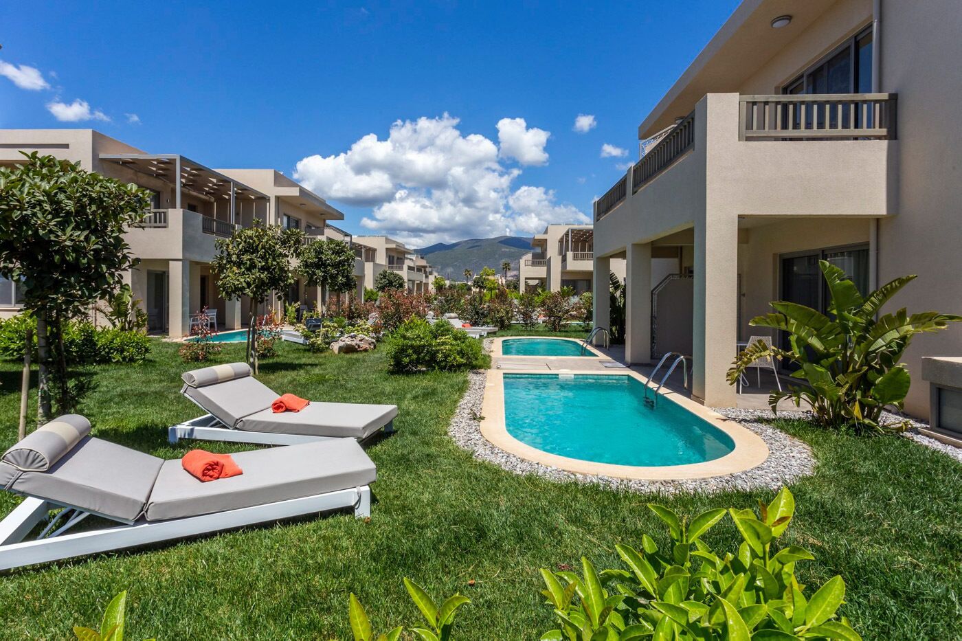 Un resort con piscina, sillas de descanso y montañas al fondo.