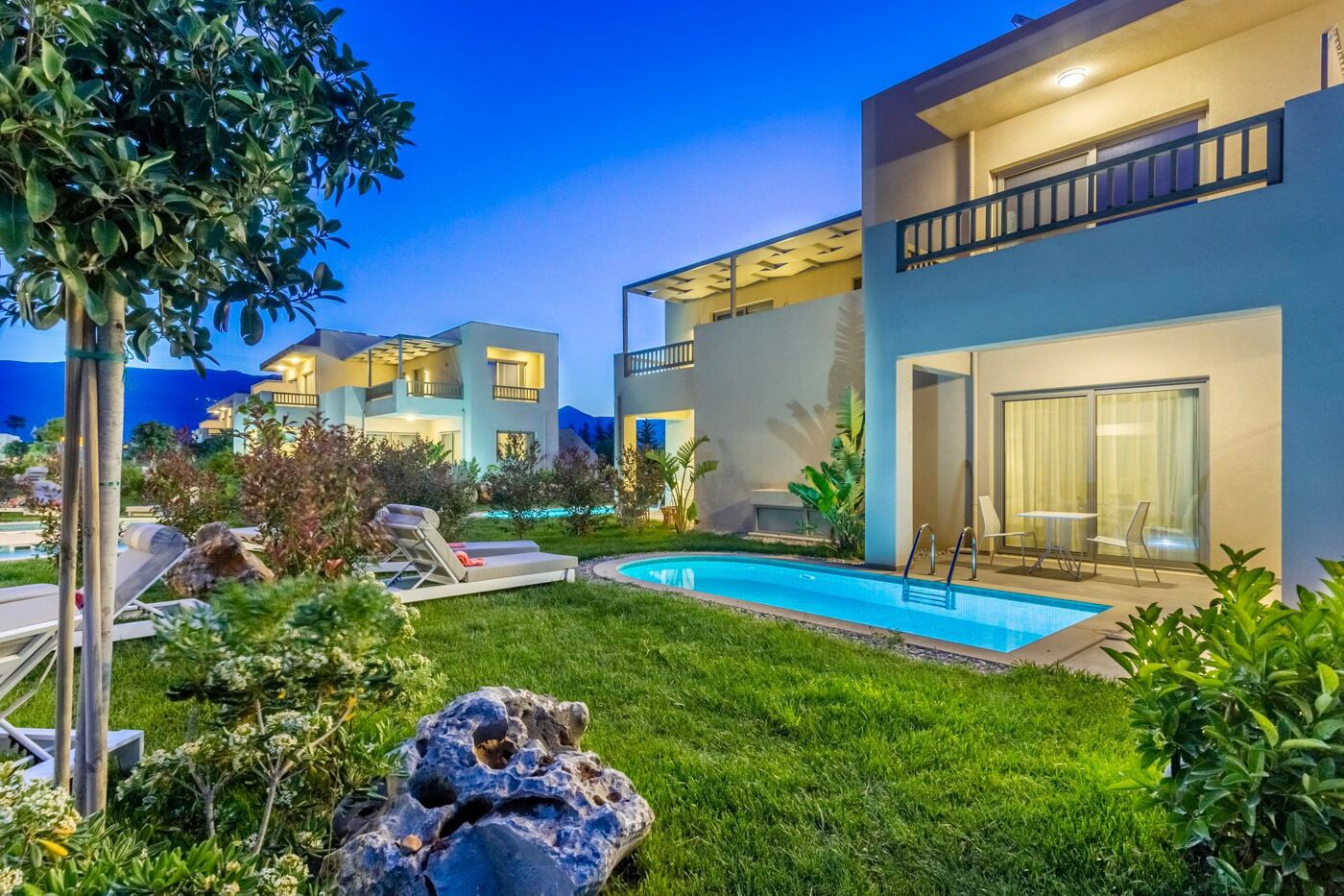 Un bâtiment moderne à deux étages doté d’une piscine, de chaises longues et d’un jardin bien entretenu.