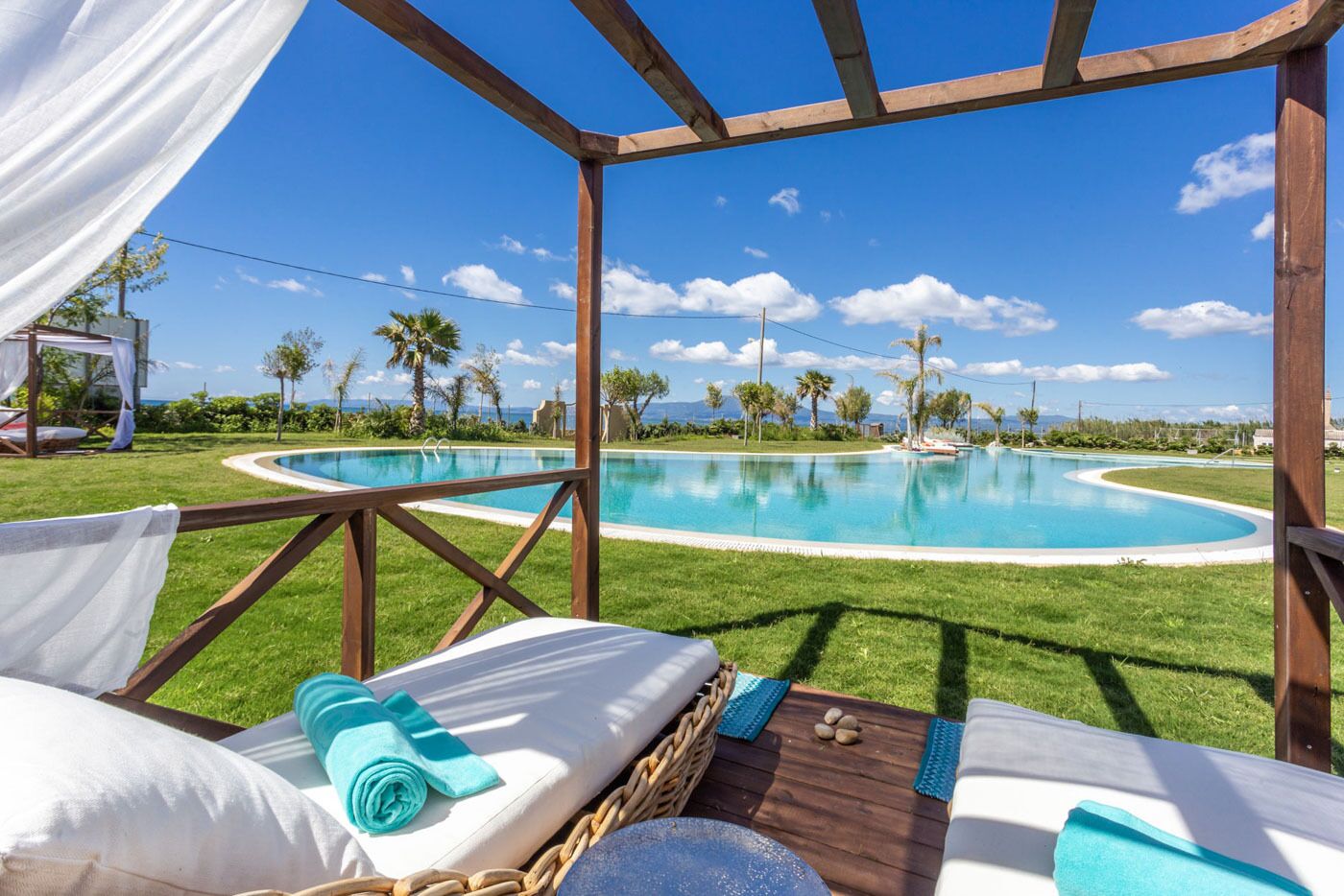 Zona junto a la piscina con una pérgola de madera, una tumbona y una mesita con una toalla y piedras.