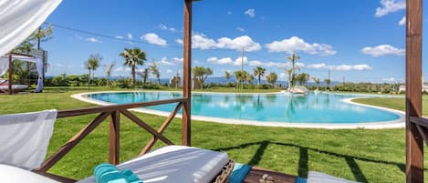 Zona junto a la piscina con una pérgola de madera, una tumbona y una mesita con una toalla y piedras.
