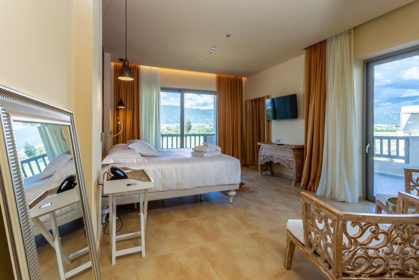 A hotel room with a bed, a desk, a chair, a TV, and a balcony with a view.
