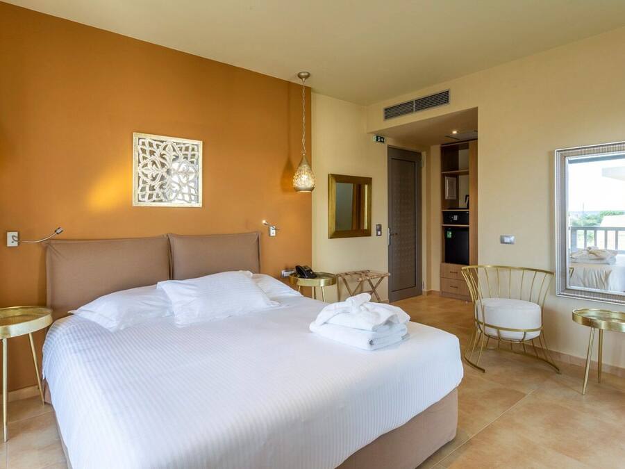 Camera d'albergo con un letto grande, una zona salotto con una sedia e un tavolino, uno specchio e vista sul balcone esterno.