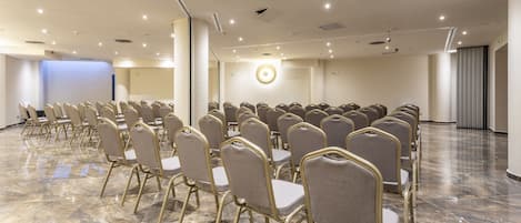 A conference room with rows of chairs, a projector screen, and a large circular light fixture on the ceiling.