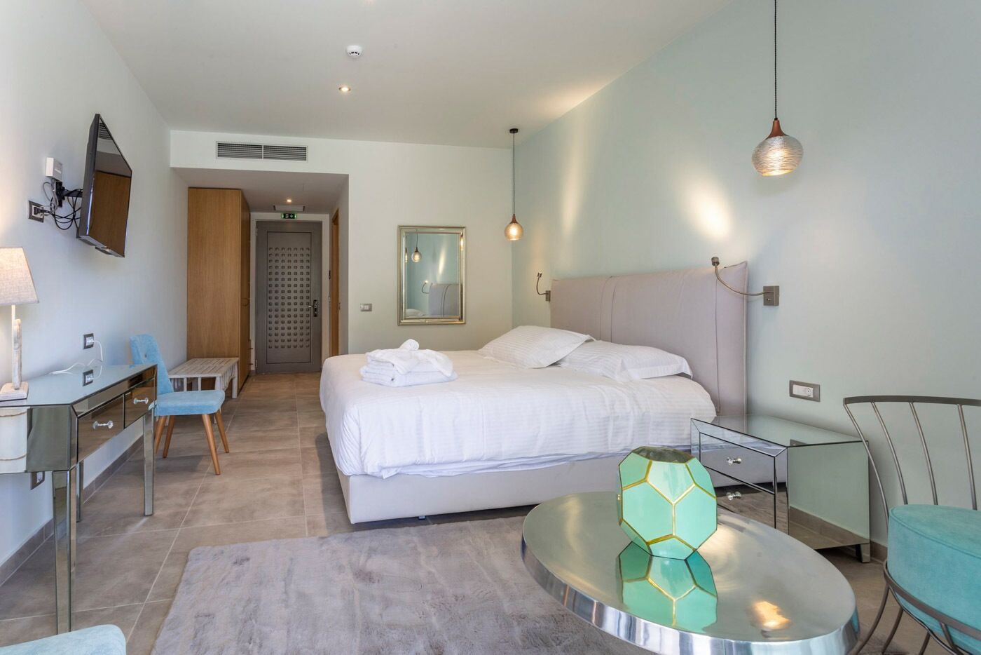 A modern hotel room with a bed, a desk, a chair, a round table, and a mirror.