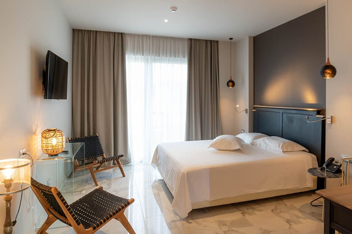 A hotel room with a bed, a desk, a chair, a TV, and a lamp.