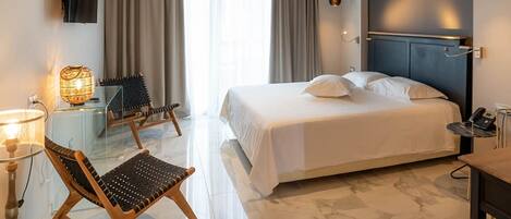 A hotel room with a bed, a desk, a chair, a TV, and a lamp.