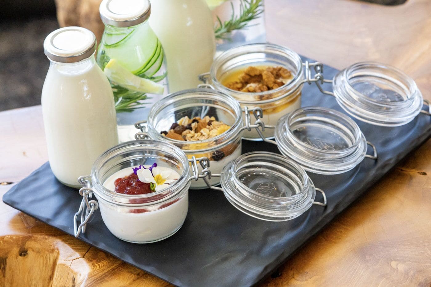 A tray with various food items, including jars of yogurt and granola, on a wooden table.