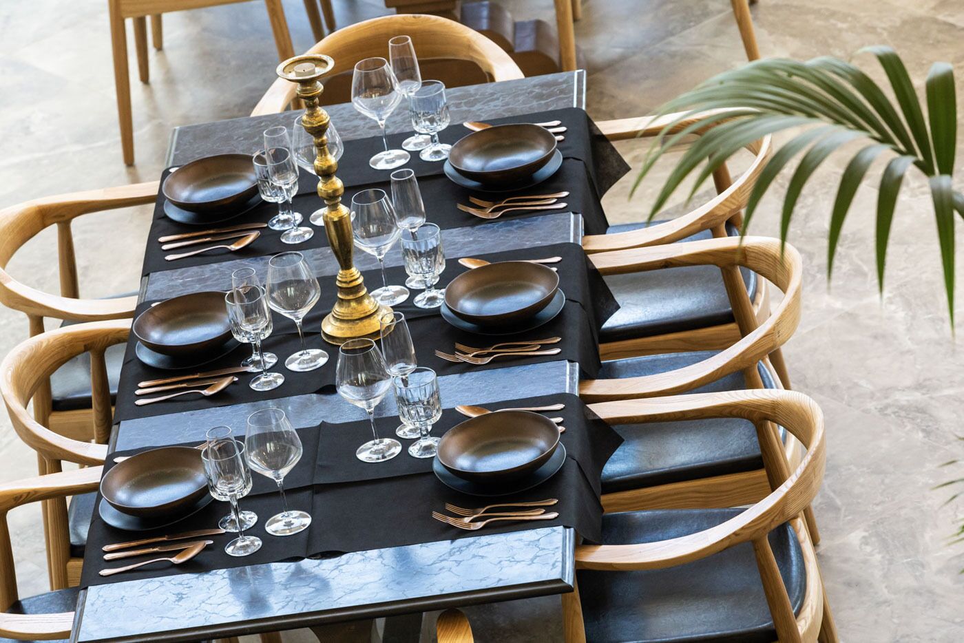 A dining table set with black tablecloth, multiple plates, glasses, and cutlery, surrounded by wooden chairs.