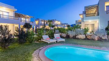 A modern hotel with a swimming pool, lounge chairs, and well-maintained gardens.