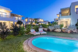 A modern hotel with a swimming pool, lounge chairs, and well-maintained gardens.