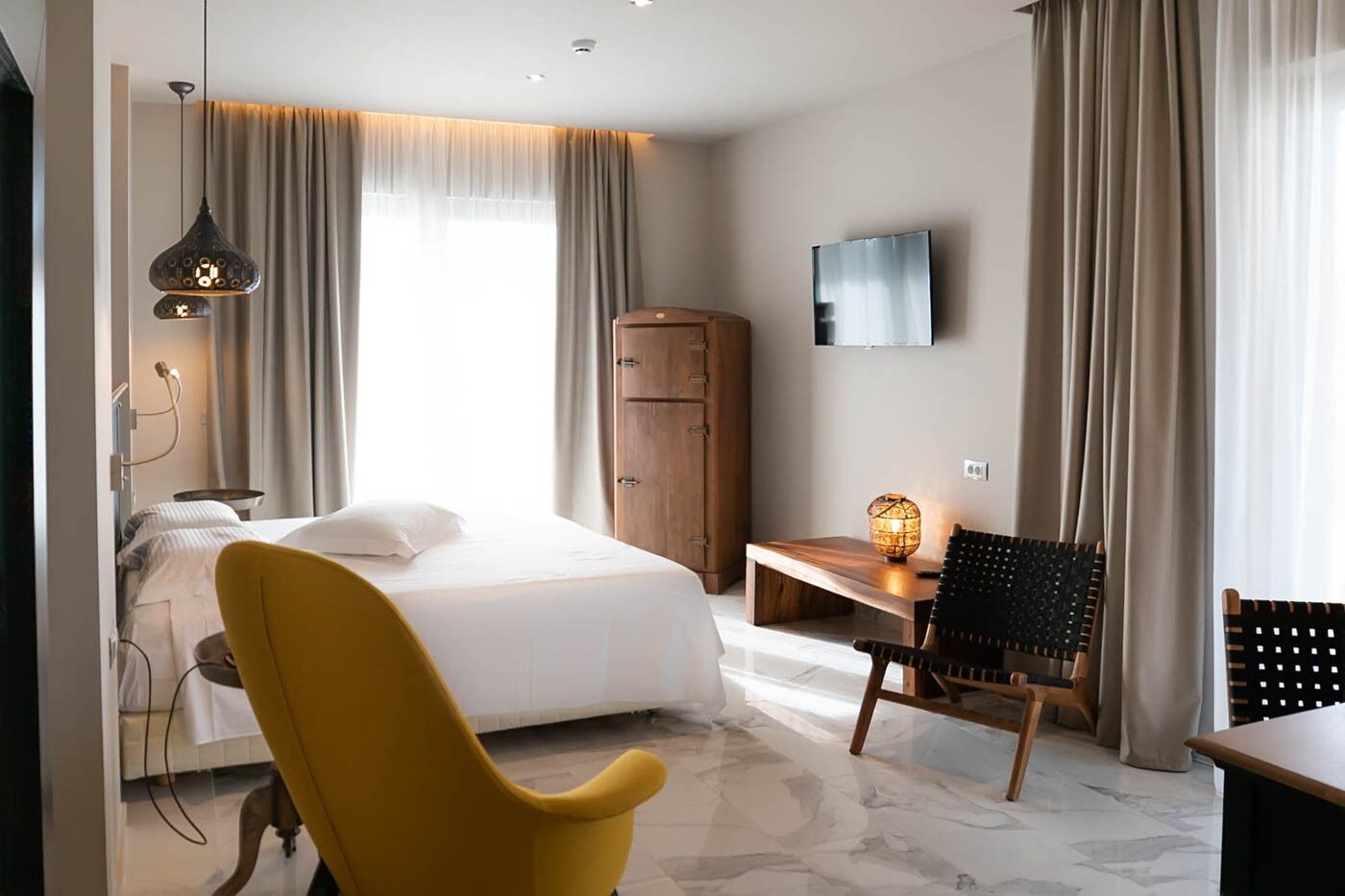 A hotel room with a bed, a desk, a chair, a wardrobe, and a TV on the wall.