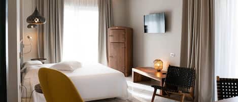 A hotel room with a bed, a desk, a chair, a wardrobe, and a TV on the wall.