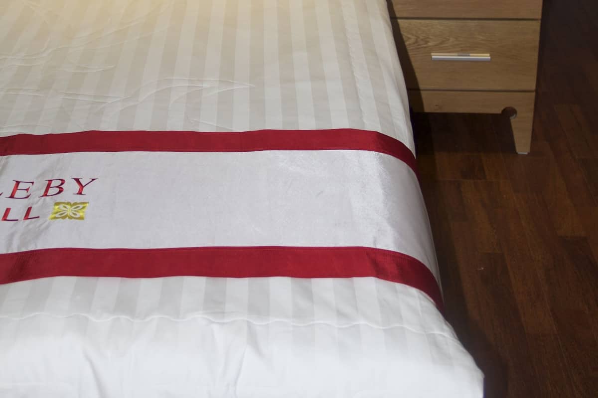 Una cama bien hecha con un edredón rojo y blanco, una almohada color beige y un cabecero de madera con diseños geométricos.