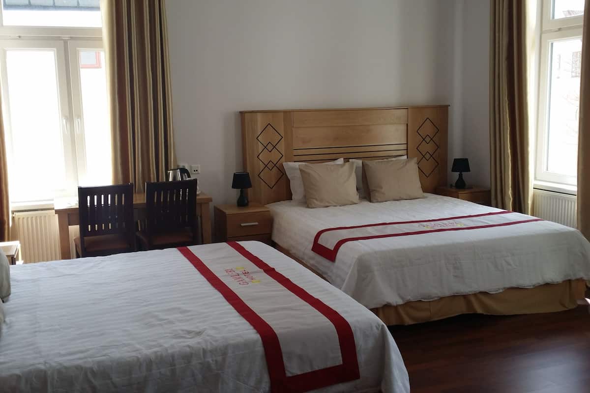 Habitación de hotel con dos camas, cabecero de madera, escritorio, silla y ventana con cortinas.