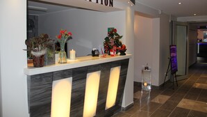 A reception desk with a 'RECEPTION' sign, a vase with red flowers, a lit candle, and a small decorative item on the counter. - Gamleby Hotell (Gamleby)