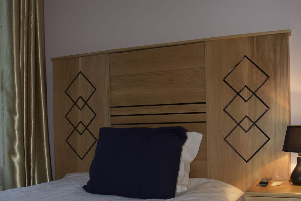 Una cama bien hecha con colcha roja y blanca, almohada azul oscuro y una mesita de noche de madera con una lámpara.