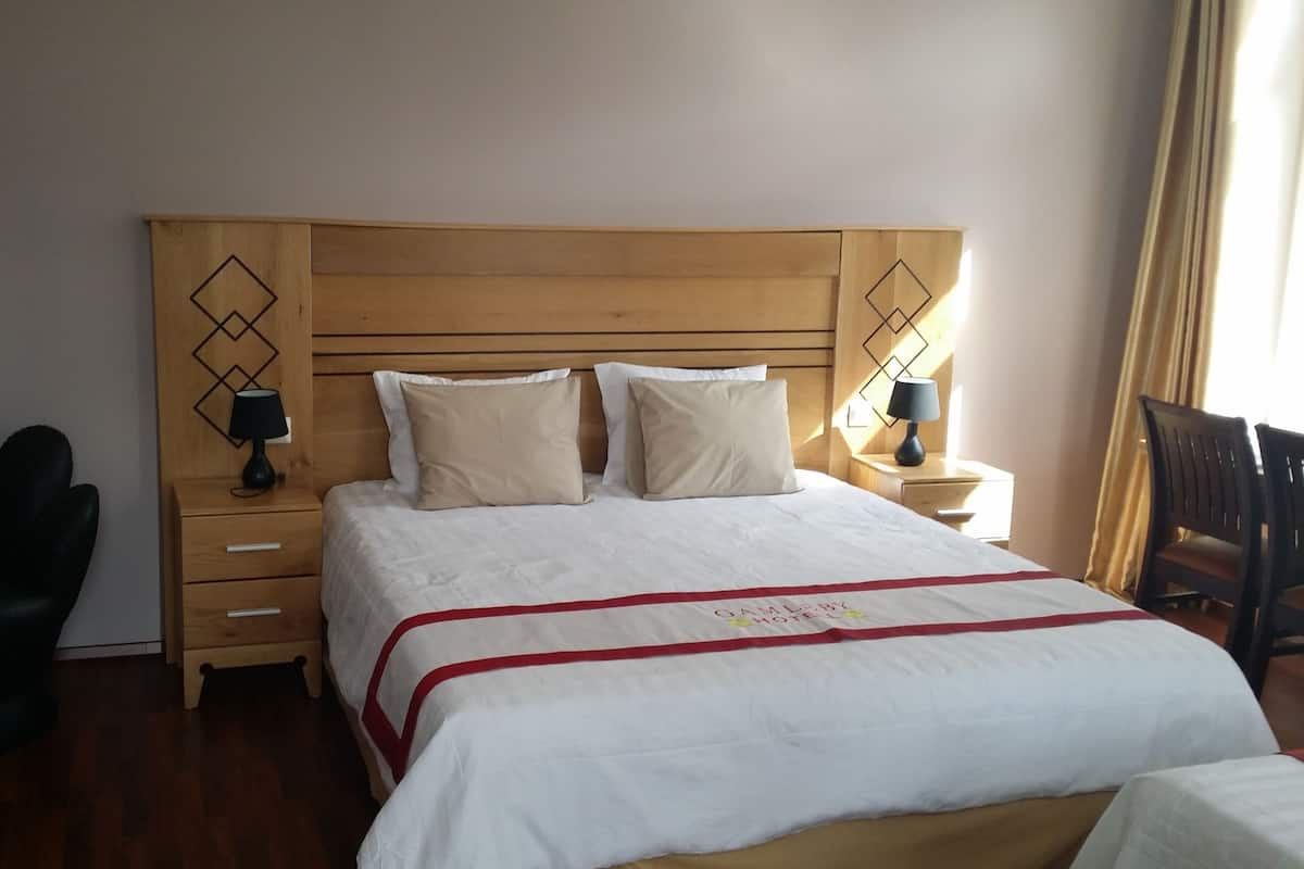 Una cama bien tendida con colcha roja y blanca, dos lámparas de noche y un cabecero de madera con diseños geométricos.