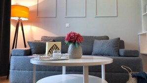Un salon avec un canapé gris, une table basse blanche, une lampe et un vase rempli de fleurs.