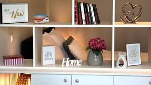 Une étagère blanche, ornée de divers objets décoratifs, notamment des livres, une horloge, des photos encadrées et un vase avec des fleurs.