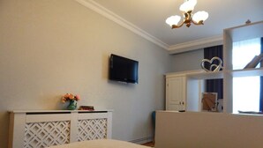 Une chambre à coucher avec un lit, un téléviseur fixé au mur, une commode et un miroir qui reflète une fenêtre.