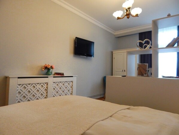 Un dormitorio con una cama, un televisor montado en la pared, un aparador y un espejo que refleja una ventana.