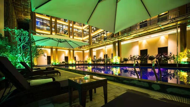 A poolside area with lounge chairs, umbrellas, and a pool reflecting the building's interior.