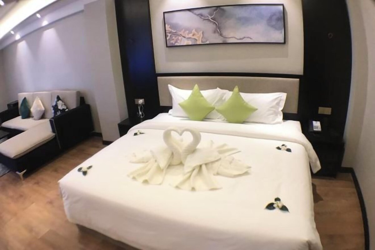 A hotel room with a neatly made bed, a sofa, and a painting on the wall.