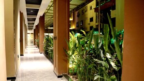 A corridor with a tiled floor, beige walls, and green plants along one side.