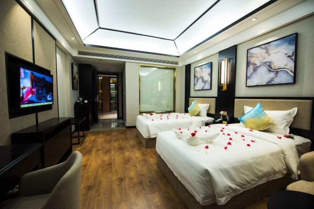 A hotel room with two beds, a TV, a desk, and artwork on the walls.