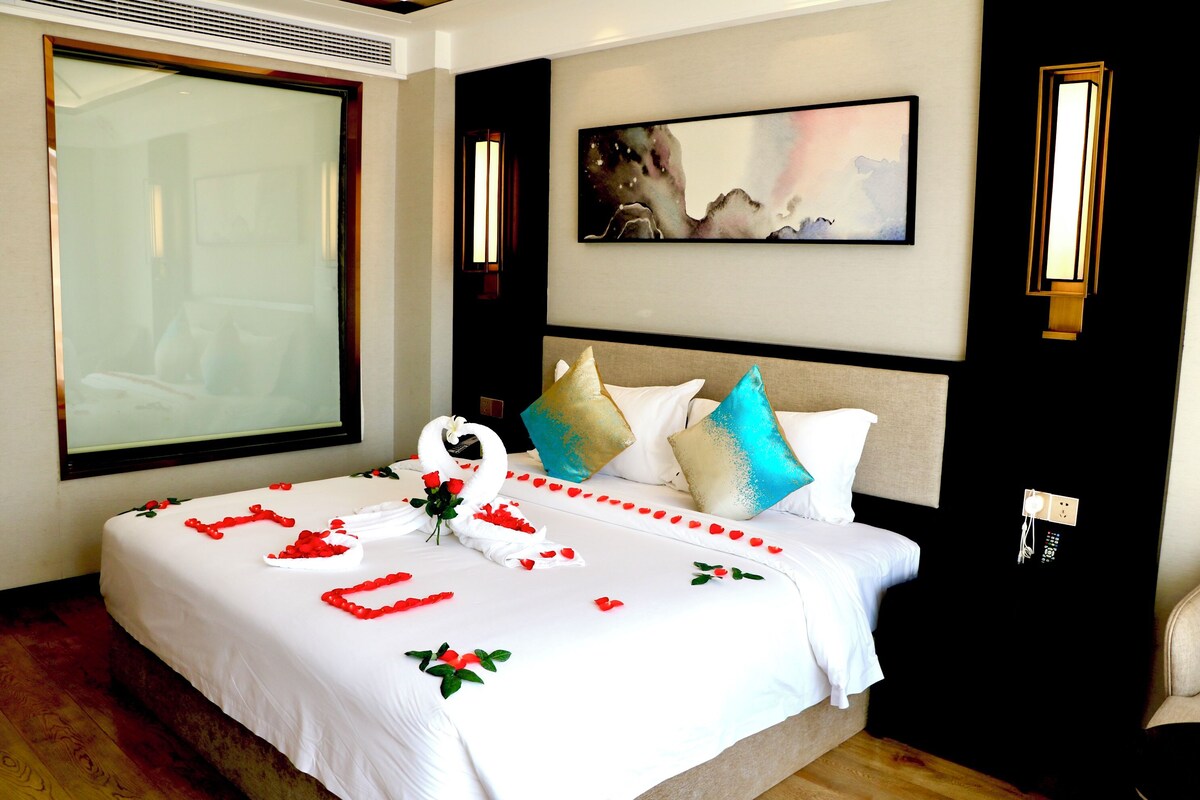 A hotel room with a large bed, a painting on the wall, and a window with a view.