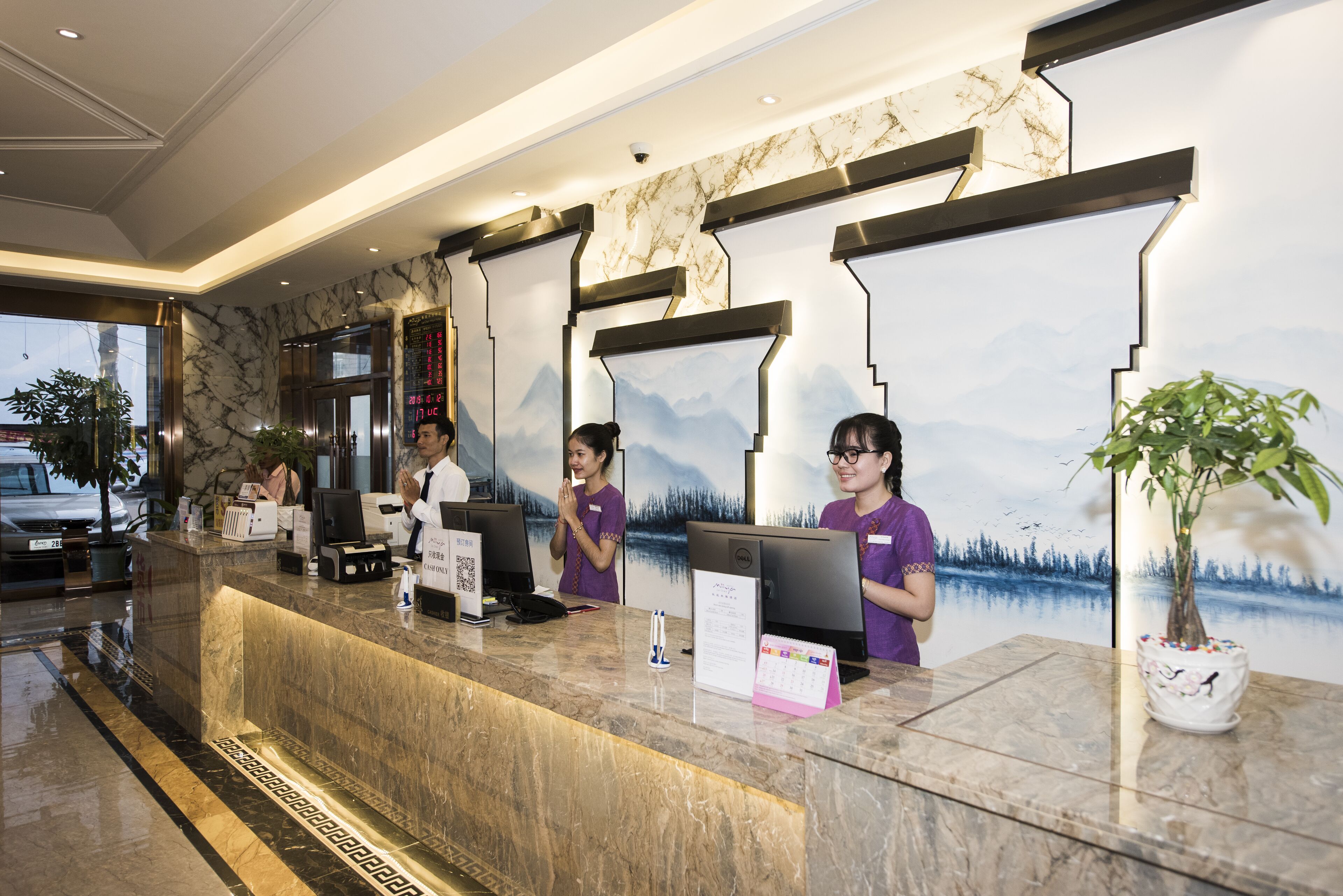 En hotelreception med en marmorbordplade, en digital skærm og et stort maleri af bjerge.