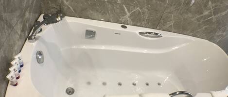 A white bathtub with a control panel, a small button, and a drain.