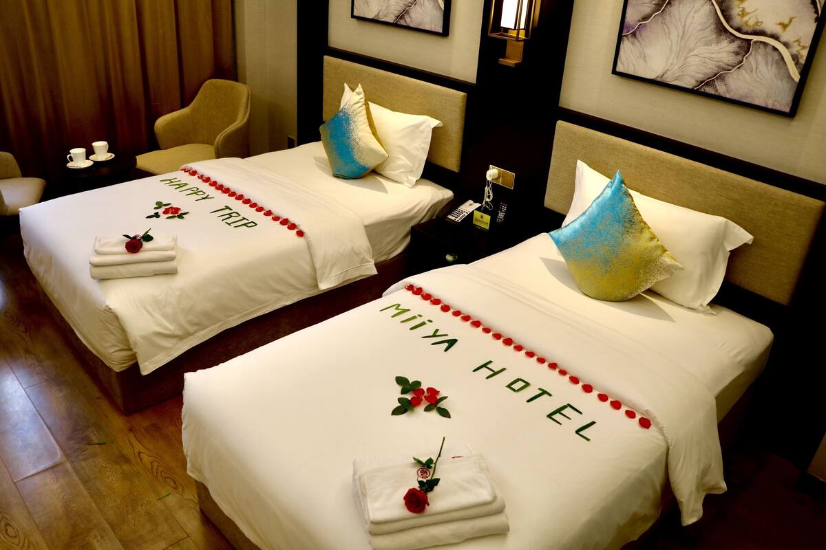 Deux lits jumeaux portant la marque « Miya Hotel », une petite table avec une tasse et une soucoupe, et une chaise.