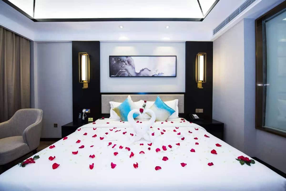 Une chambre d’hôtel moderne avec un grand lit, une chaise, un tableau au mur et deux lampes fixées au mur.
