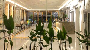 A modern hotel lobby with a glass partition, a reception desk, and seating areas.