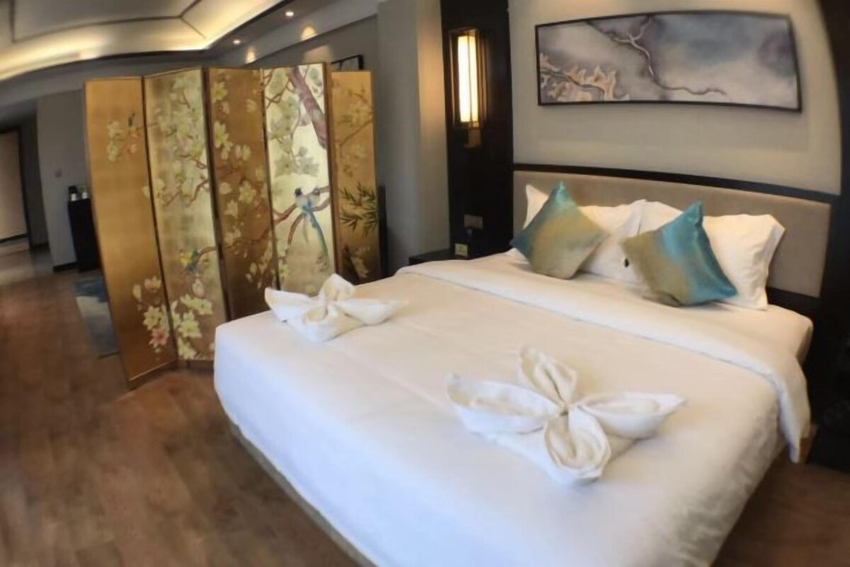 A hotel room with a large bed, a decorative screen, and a painting on the wall.