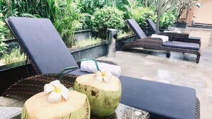 A poolside area with lounge chairs and two coconuts with flowers on a glass table.