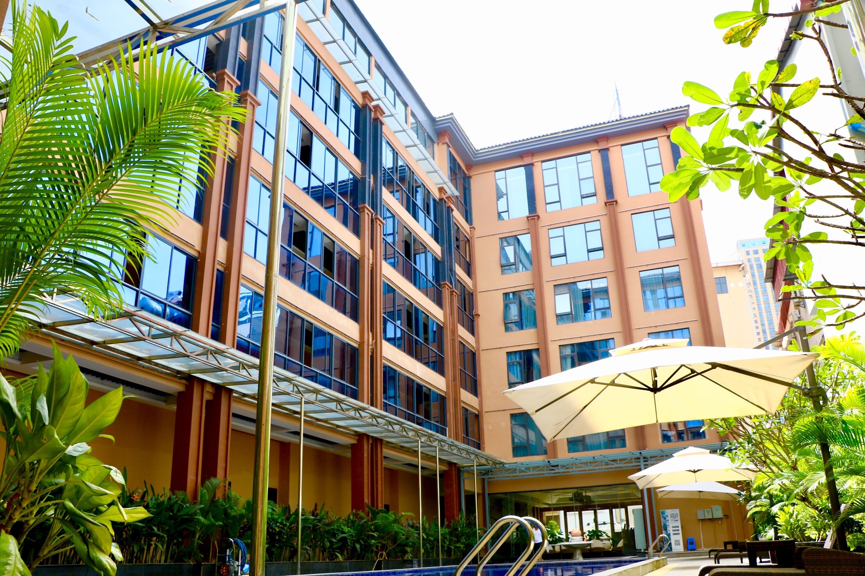 A modern hotel with a glass atrium, outdoor seating, and lush greenery.