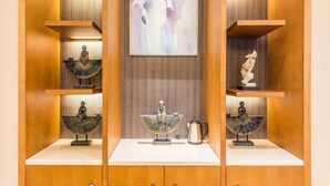 Ein Zimmer mit Holzvertäfelung, drei Regalen mit Statuen, einem zentralen Kunstwerk und einer Kaffeemaschine auf der Arbeitsfläche.