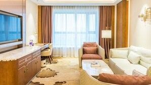 Ein modernes Hotelzimmer mit Flachbildfernseher, einer Couch, einem Sessel, einem kleinen Tisch und einem Schreibtisch mit Lampe.