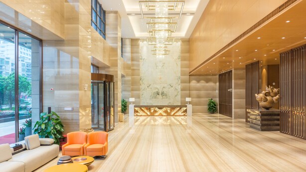 Eine geräumige Lobby mit einer Rezeption, einer Sitzecke und großen Fenstern mit Blick ins Freie.