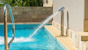 A swimming pool with clear blue water, a metal ladder, and a stone wall in the background. - Apartments Aura - Comfort Studio Apartment f with shared swimming pool (Dubrovnik)