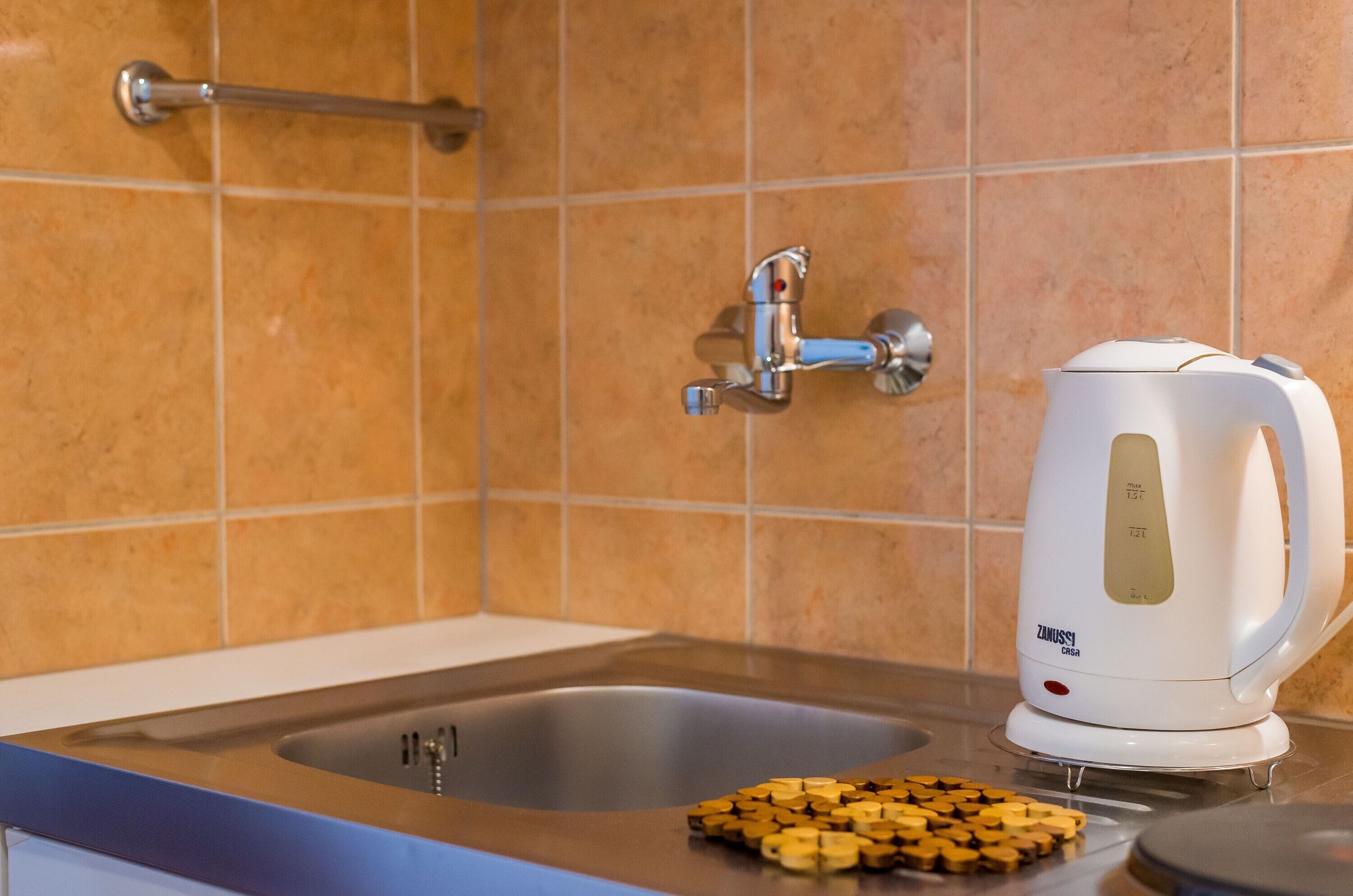 Eine Küche mit Spüle, Wasserhahn und einem weißen Wasserkocher auf der Arbeitsfläche.